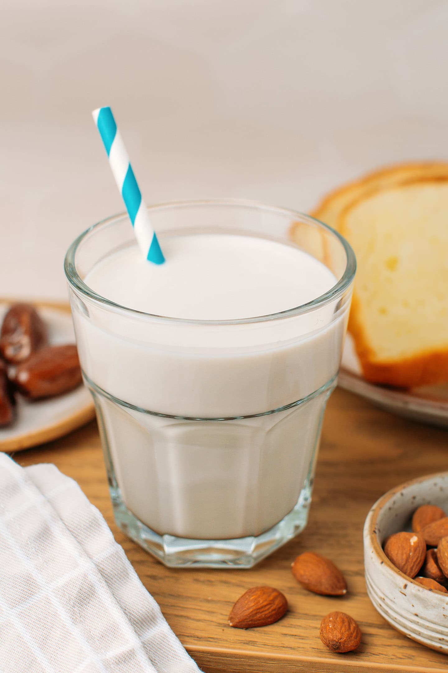 Glass of homemade almond milk with a blue straw on a wooden board.