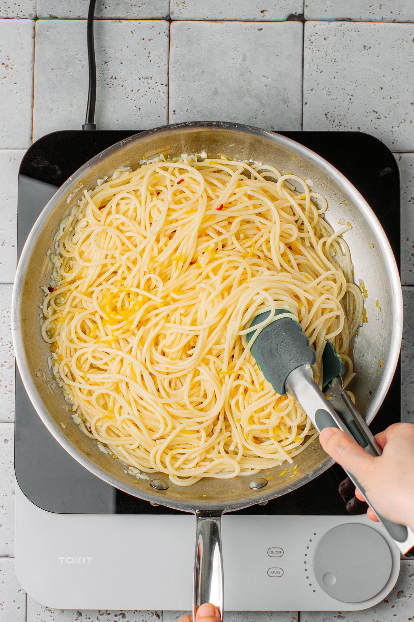 Tossing spaghetti with butter and lemon zest in a skillet.