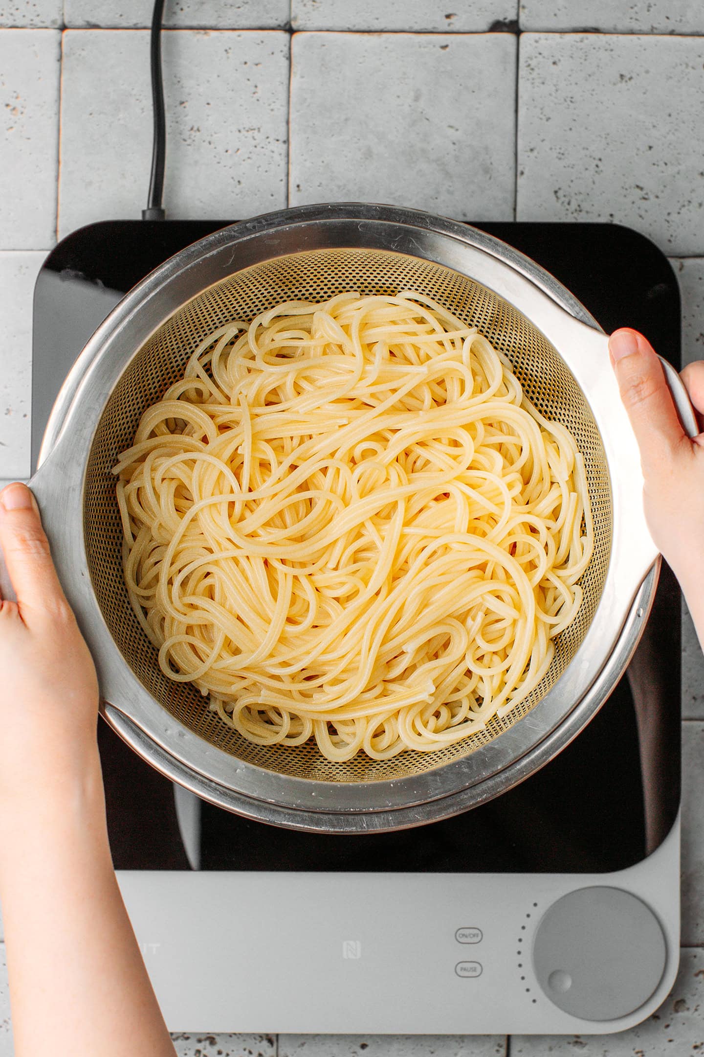 Draining cooked spaghetti using a colander.