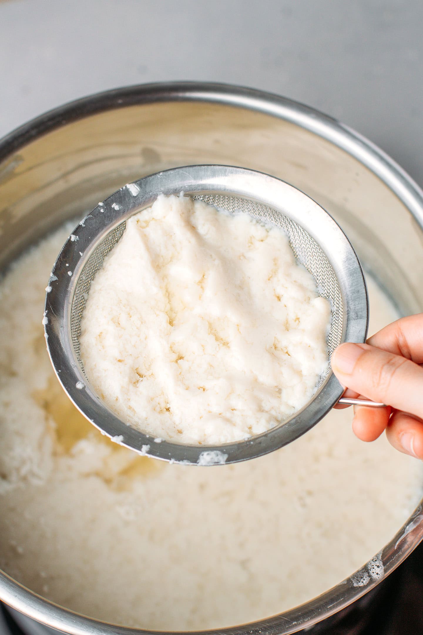 Holding a five-mesh sieve to scoop out curds.