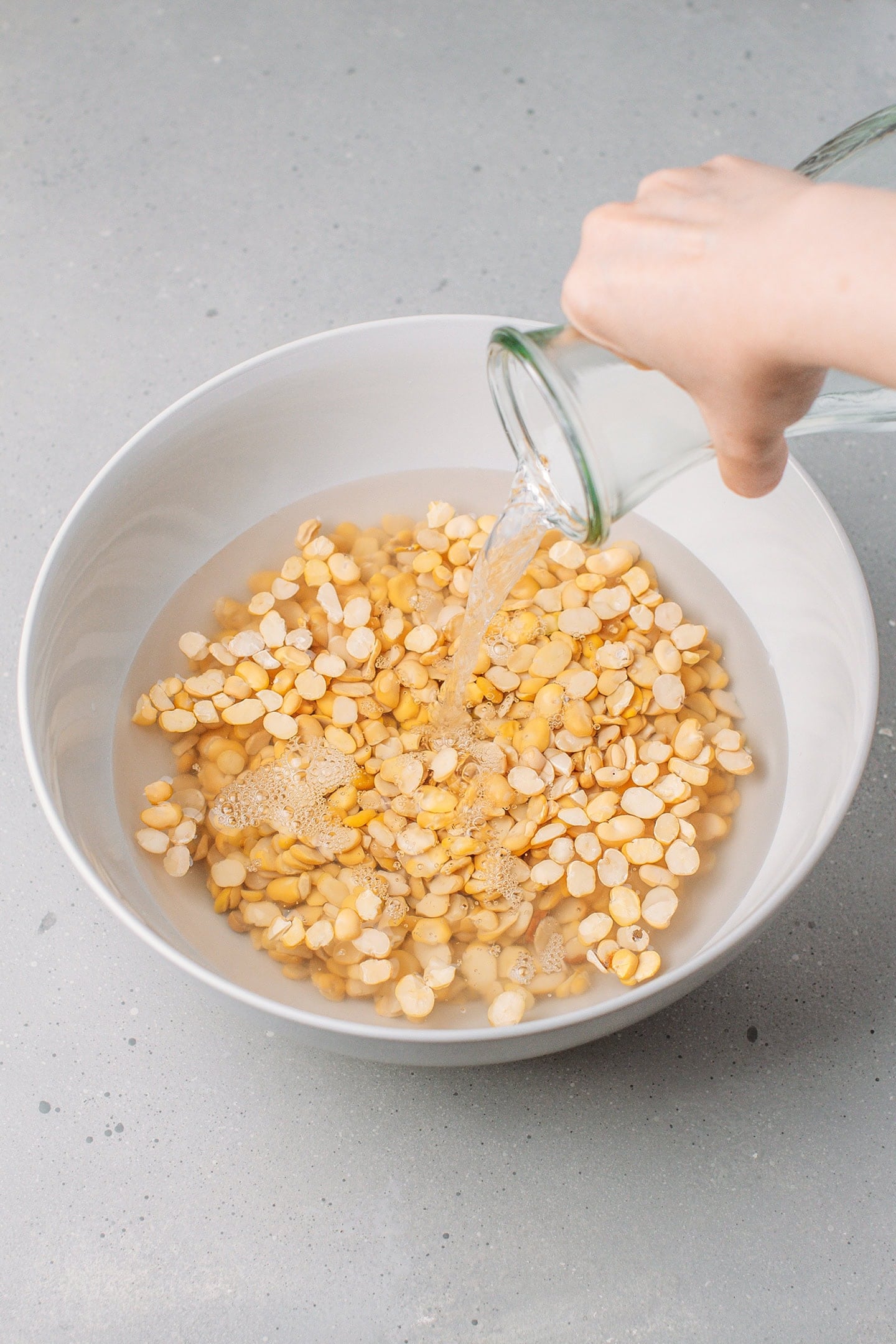 Pouring water into a bowl containing fava beans.