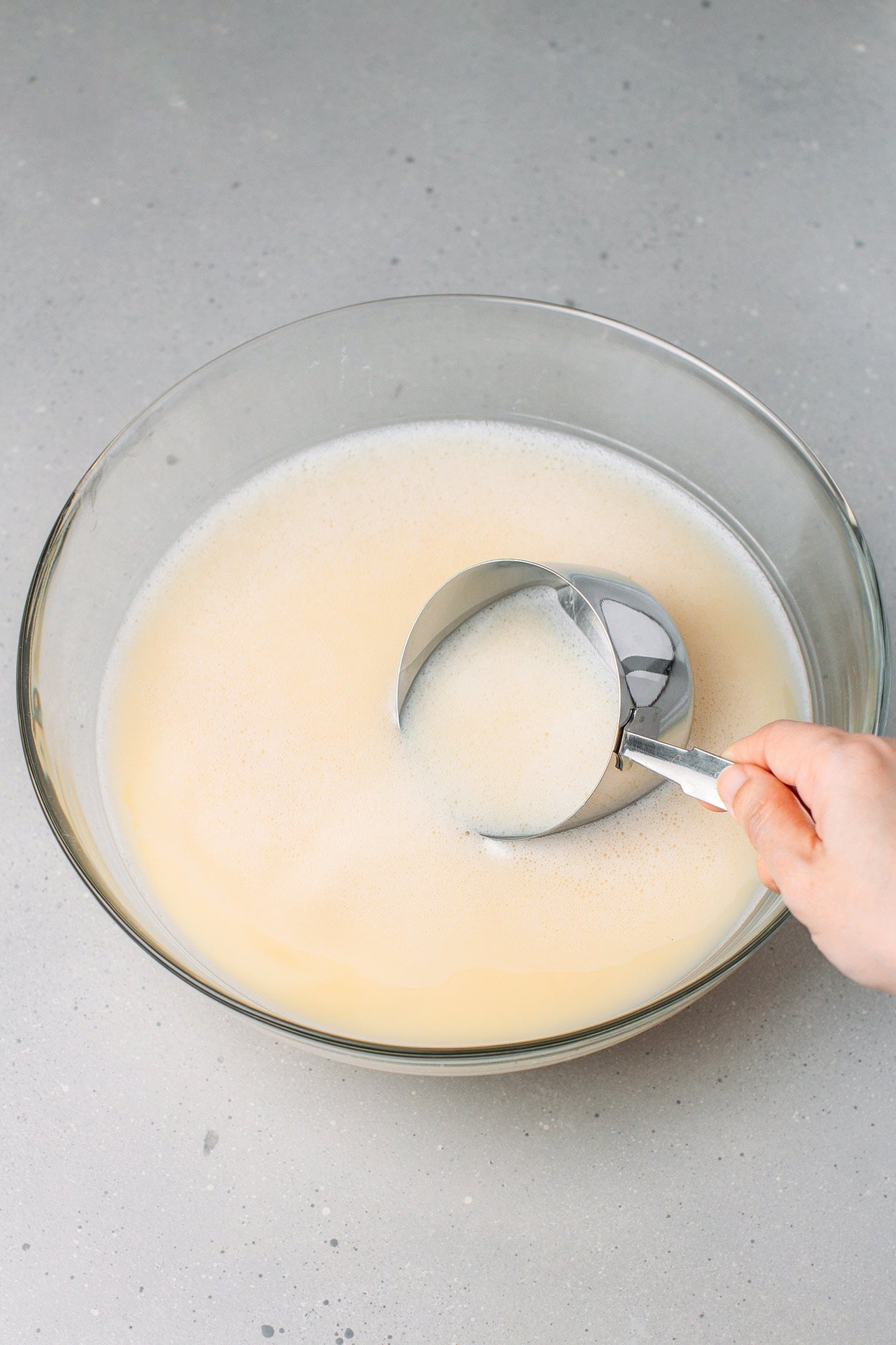 Scooping out fava bean milk using a measuring cup.