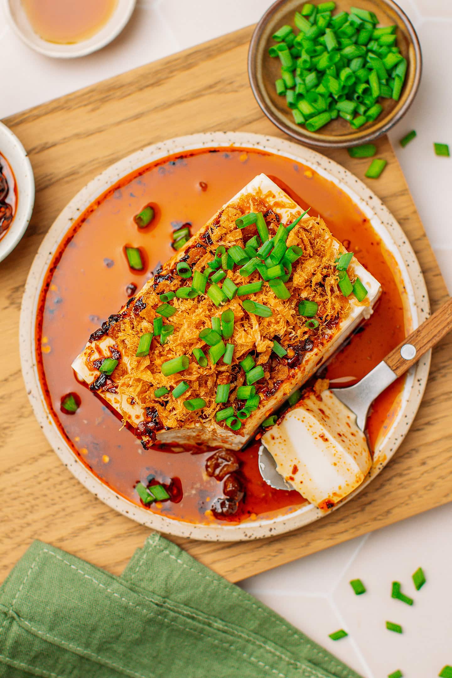 Top view of a block of silken tofu topped with chili crisp, vegan meat floss, and green onions.